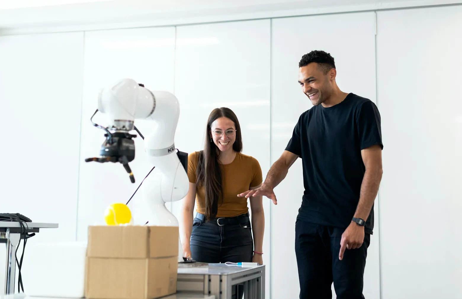 Two colleagues working beside a robotic arm in a bright workspace